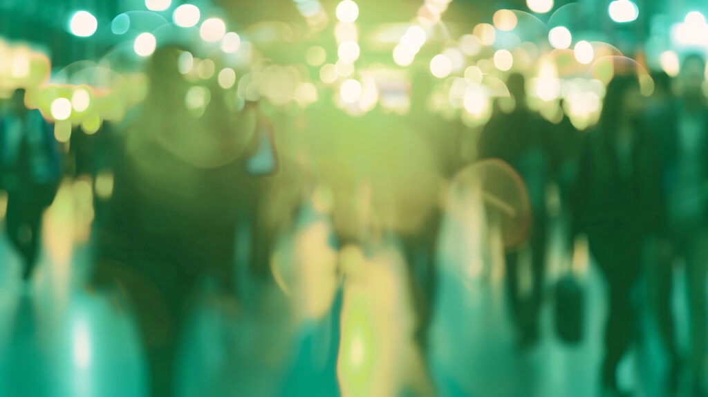 Unschärfe einer Menschenmenge in einer Veranstaltungshalle mit grünlichen Lichtern im Hintergrund.